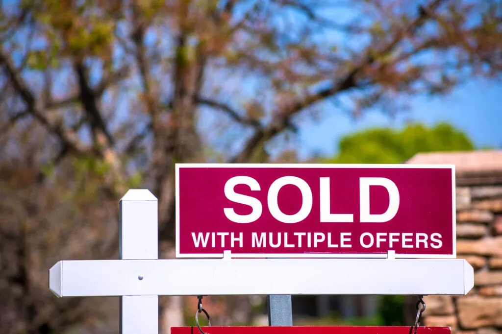 sold with multiple offers real estate sign near purchased house indicates hot seller's market in the desired neighborhood. blurred outdoor background