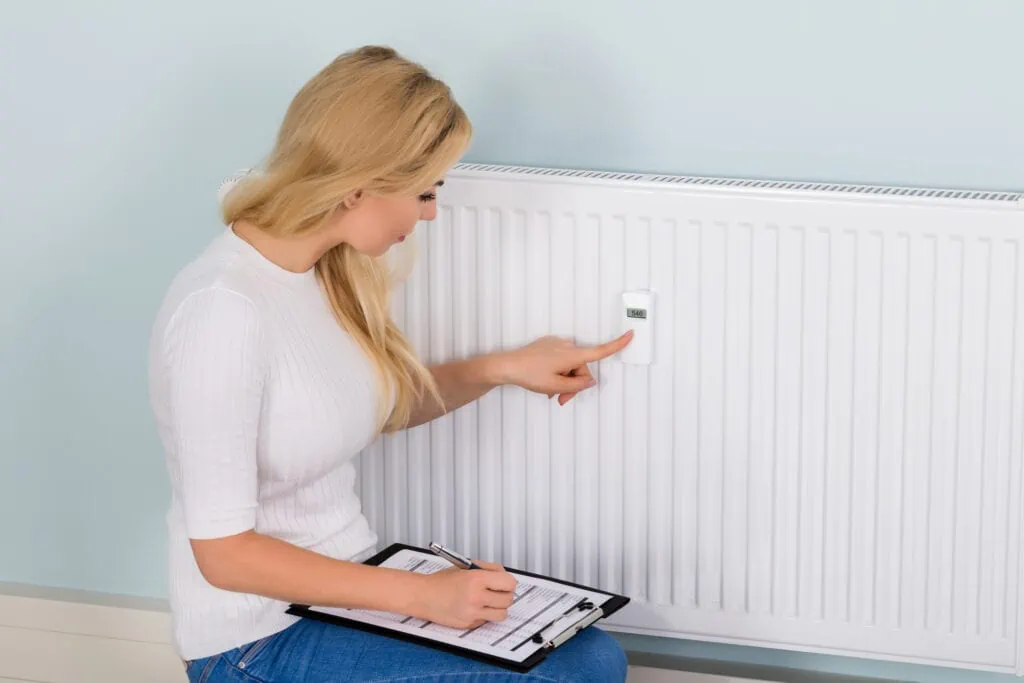 woman with clipboard checking digital thermostat